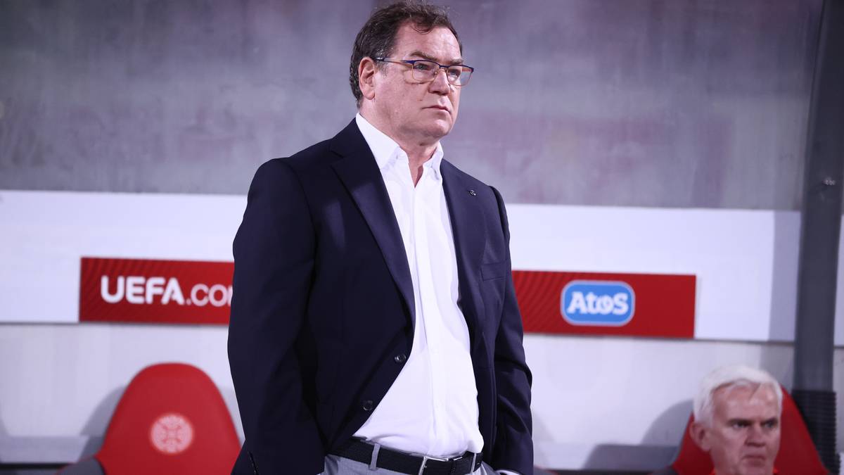 Mężczyzna w garniturze i okularach stoi, patrząc w bok.