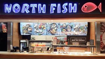 Neonowy napis "NORTH FISH" nad ladą z ekspozycją potraw i ekspozycją lod&oacute;w z owocami