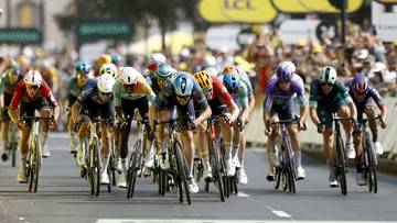 Peleton kolarzy finiszuje na etapie wyścigu, z widocznymi numerami startowymi na koszulkach.