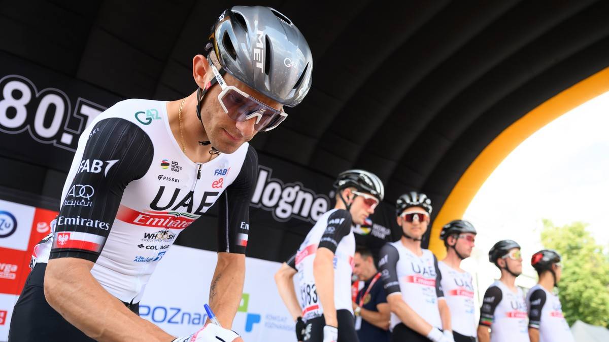 Kolarz w kasku i okularach przeciwsłonecznych, ubrany w koszulkę kolarską zespołu UAE Emirates, przygotowuje się do startu.