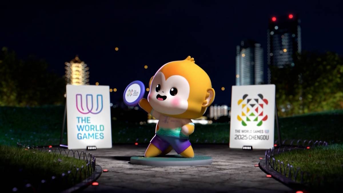 Ilustracja maskotki Małpki z The World Games 2025 trzymająca w dłoni okrągły, niebieski medalion. Za nią znajdują się dwie plansze z logotypami wydarzenia.