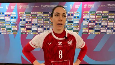 Monika Kobylińska, zawodniczka piłki ręcznej, w czerwonej koszulce z numerem 8 i godłem Polski, udziela wywiadu na tle ściany z logotypami.