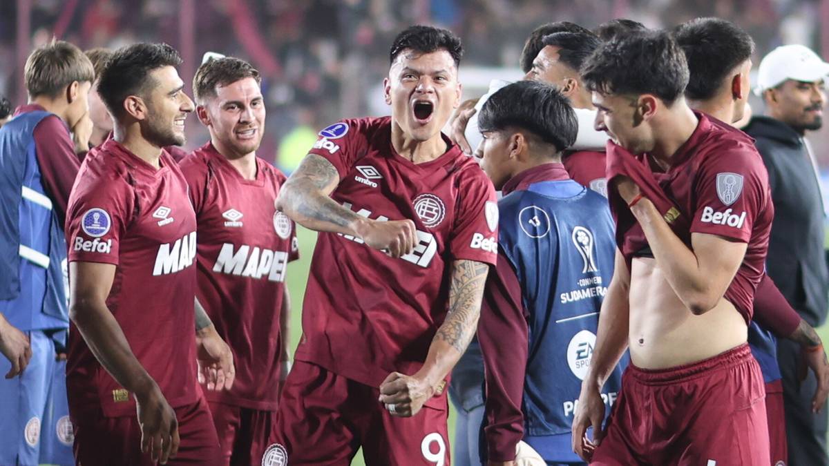 Piłkarze w bordowych strojach, jeden krzyczy z radości, otoczony przez kolegów z drużyny, świętujący awans do finału Copa Sudamericana.