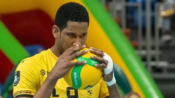 Siatkarz w ż&oacute;łtej koszulce z numerem 9 trzyma piłkę do siatk&oacute;wki przed twarzą w geście koncentracji.