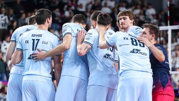 Siatkarze drużyny PGE Projekt Warszawa świętujący po zdobyciu punktu, stojący w zwartej grupie w jasnych strojach.