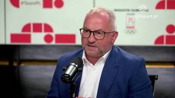 Grzegorz Bachański w marynarce i okularach siedzi przed mikrofonem, udzielając wywiadu.