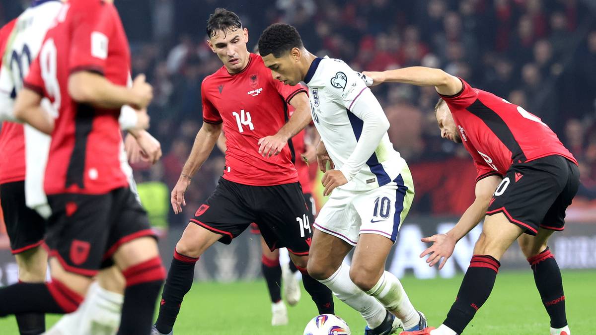 Piłkarze w czerwonych i białych strojach rywalizują o piłkę na boisku piłkarskim.