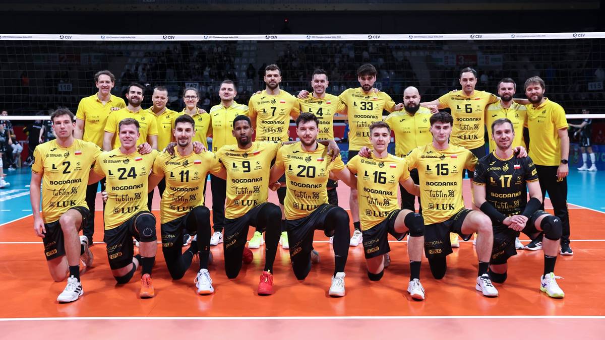 Drużyna siatkarska w ż&oacute;łtych strojach pozuje do zdjęcia na boisku.