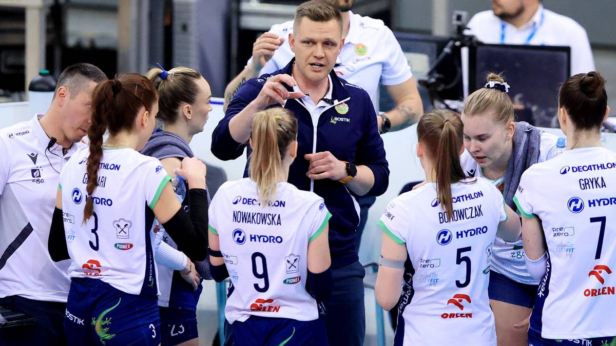 Trener udziela wskaz&oacute;wek grupie siatkarek w strojach sportowych.