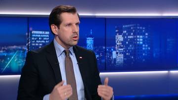 Mężczyzna w garniturze i krawacie siedzi i gestykuluje podczas wywiadu w studiu telewizyjnym.