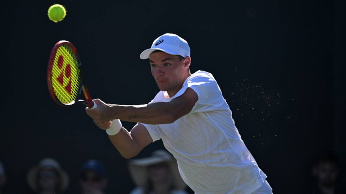 Tenisista w białej koszulce i czapce z daszkiem odbija piłkę rakietą podczas meczu na kortach Wimbledonu.