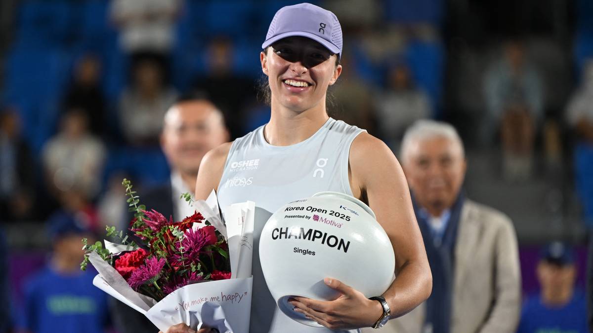 Iga Świątek w koszulce sportowej i czapce z daszkiem trzyma puchar zwycięzcy turnieju tenisowego w Seulu. Uśmiecha się szeroko.