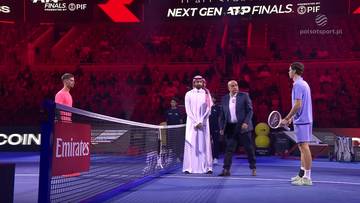 Dwaj tenisiści, Alexander Blockx i Dino Prizmic, stoją po przeciwnych stronach kortu tenisowego, przy siatce. Obok nich znajduje się sędzia i inna osoba w tradycyjnym stroju.