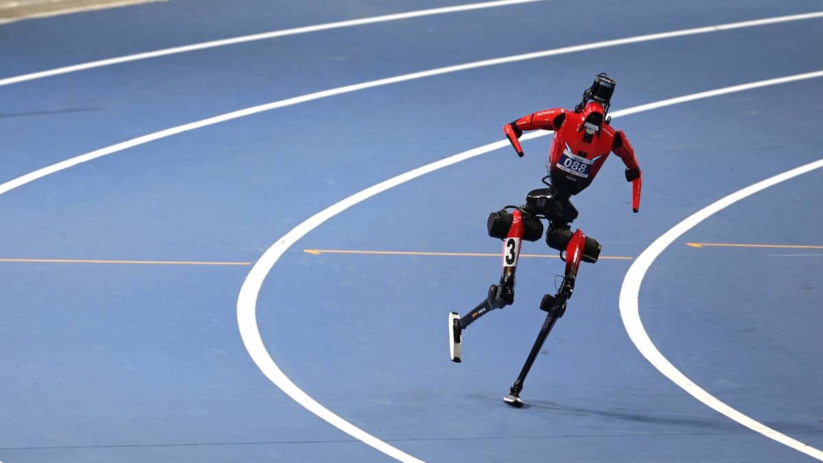 Robot w czerwono-czarnej zbroi z protezami nóg biegnie po niebieskiej bieżni lekkoatletycznej.
