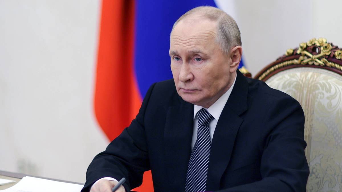 Władimir Putin siedzi przy stole, pisząc coś na kartce.