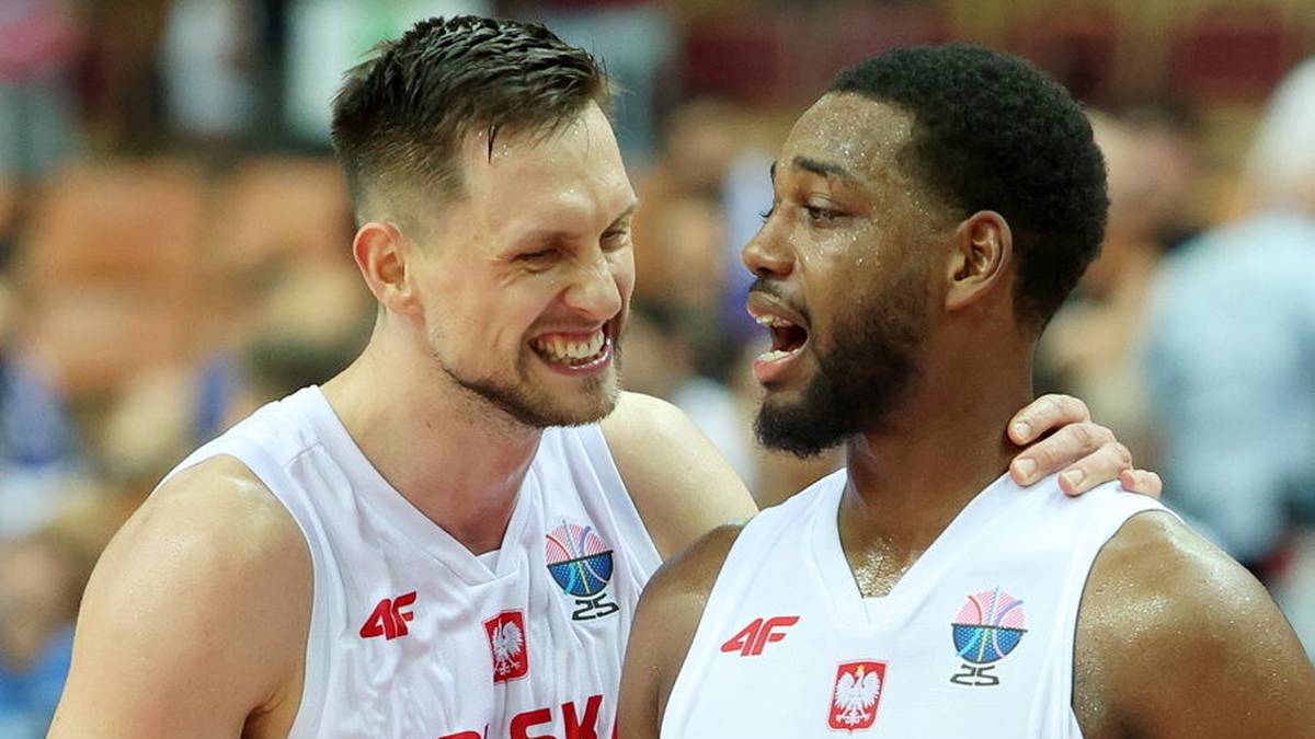 Dwóch koszykarzy reprezentacji Polski w białych koszulkach, jeden z nich śmieje się, drugi patrzy w bok.