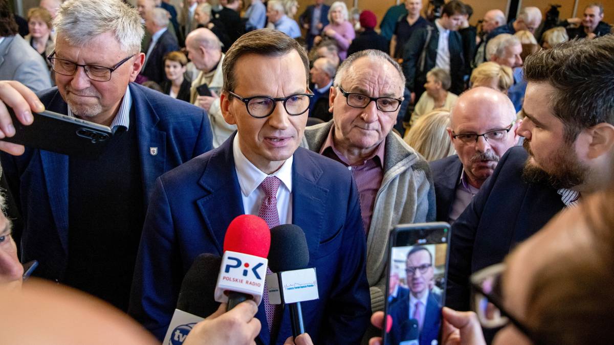 Mateusz Morawiecki w okularach i garniturze odpowiada na pytania dziennikarzy trzymających mikrofony.