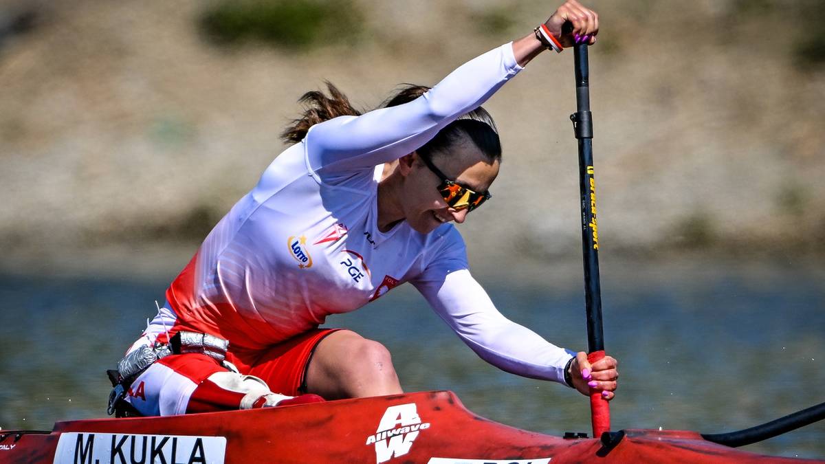 Kobieta w czerwono-białej kamizelce sportowej i szortach wiosłuje w kajaku.