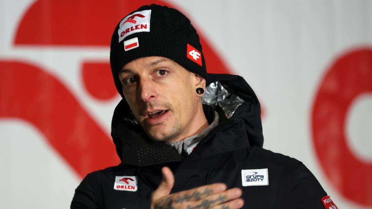 Mężczyzna w czapce z logo Orlen, ubrany w ciemną kurtkę, rozmawia, wskazując ręką.