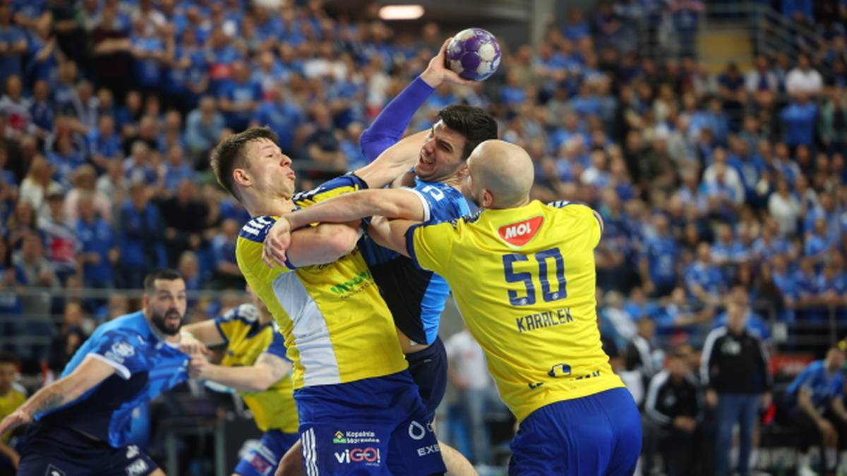 Piłkarze ręczni walczą o piłkę w trakcie meczu na pełnej trybunie.