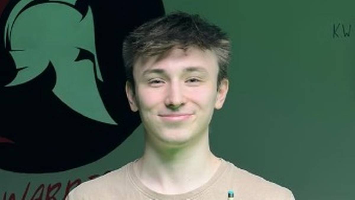 Portret młodego mężczyzny, prawdopodobnie snookerzysty, z uśmiechem na twarzy. W tle widoczne jest logo z greckim hełmem.