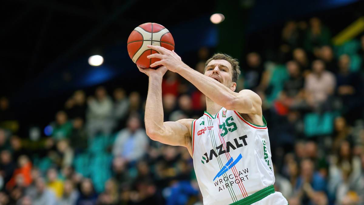 Koszykarz w białym stroju z numerem 35 rzuca do kosza, broniony przez zawodnika w niebieskim stroju.