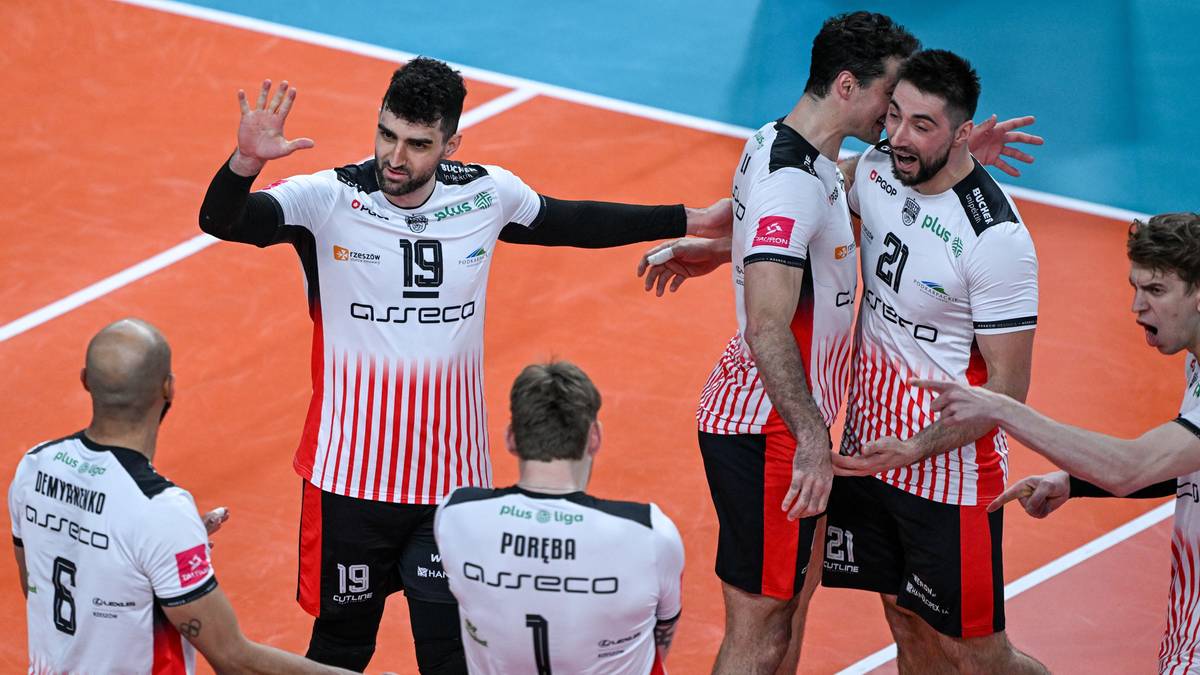 Siatkarze Asseco Resovii Rzeszów w białych strojach z czerwonymi pasami, jeden z nich unosi rękę w geście radości, podczas meczu.