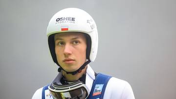 Portret skoczka narciarskiego w białym kasku i goglach narciarskich.