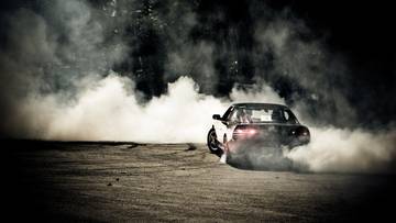 Samoch&oacute;d wykonujący drift, otoczony gęstym dymem z palonych opon w ciemności.