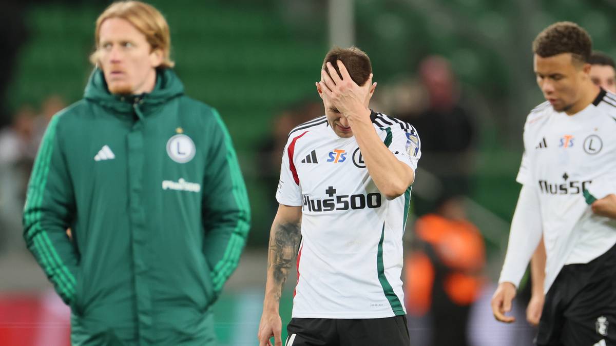 Trzech piłkarzy Legii Warszawa, jeden w zielonej kurtce treningowej, dwaj w białych koszulkach, jeden z nich trzyma się za czoło.