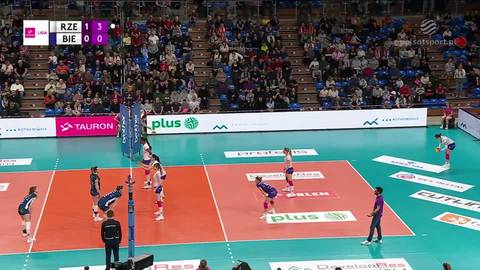 Grający w siatk&oacute;wkę zawodnicy na boisku, w tle trybuny z kibicami.