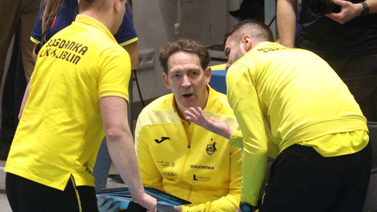 Trener w środku, otoczony przez dw&oacute;ch zawodnik&oacute;w, wszyscy w ż&oacute;łtych strojach sportowych, dyskutują.