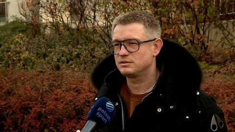 Przemysław Pawlak w okularach i czarnej kurtce z kapturem, udziela wywiadu dla Polsat Sport na tle krzewów.