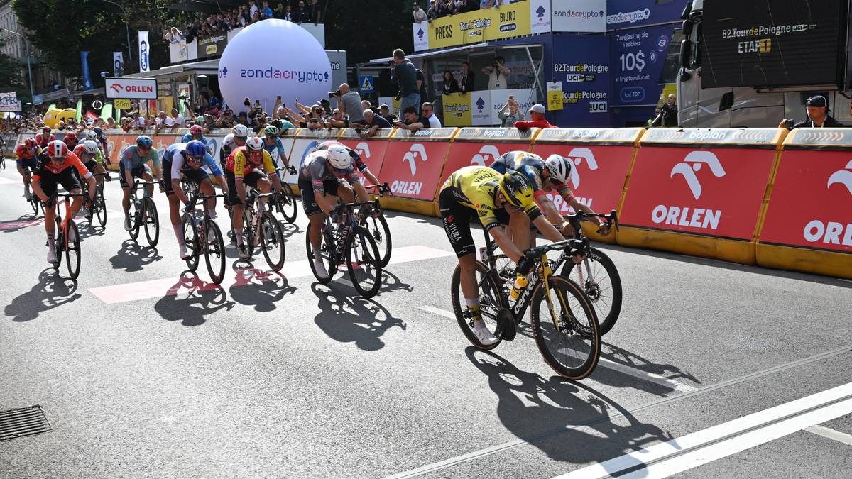 Grupa kolarzy ściga się na drodze, jeden z kolarzy leży na asfalcie po wypadku.