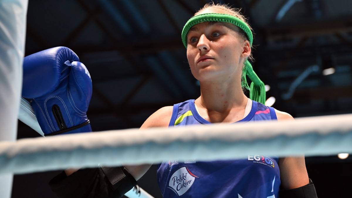 Portret Martyny Kierczyńskiej w podczas walki muay thai. Ma na głowie opaskę w kolorze zielonym, a na dłoniach niebieskie rękawice bokserskie.