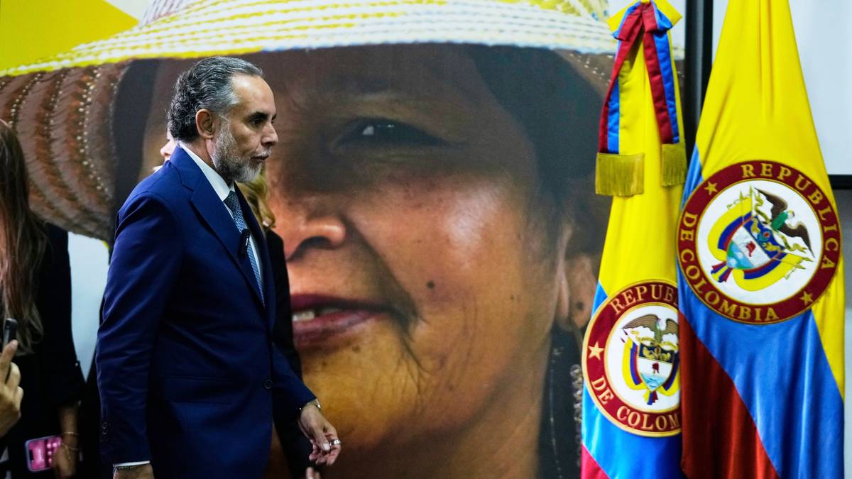 Mężczyzna w garniturze idzie obok flag Kolumbii i plakatu z wizerunkiem kobiety.
