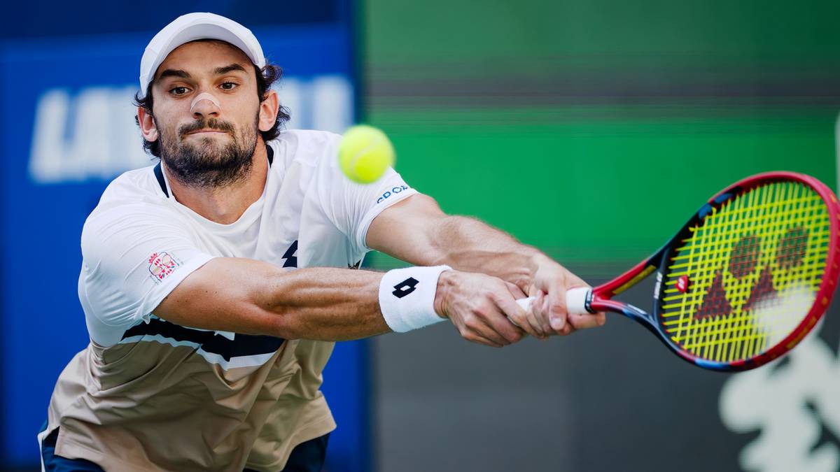 Tenisista w białej czapce i białej koszulce uderza piłkę rakietą.