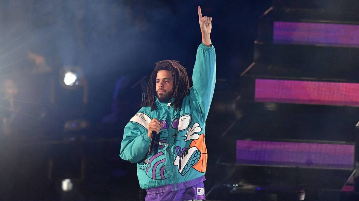 Raper J. Cole występuje na scenie, wskazując palcem w g&oacute;rę przed publicznością.