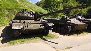 Kilka starych czołgów i pojazdów opancerzonych w kolorze zielonym, stojących na trawiastym podłożu.