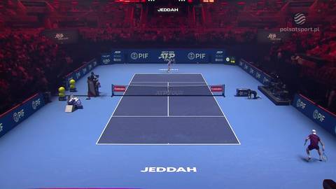 Widok kortu tenisowego z zawodnikami podczas meczu. Na niebieskiej nawierzchni z widocznym logo "JEDDAH" rozgrywa się spotkanie między Alexandrem Blockx a Nicolaiem Budkovem Kjaere.