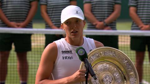 Iga Świątek w białej czapce i koszulce z logo "Infosys" trzyma trofeum tenisowe.