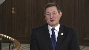 Poseł Kamil Wnuk z partii Polska 2050 w czarnym garniturze i granatowym krawacie, m&oacute;wiący do kamery.