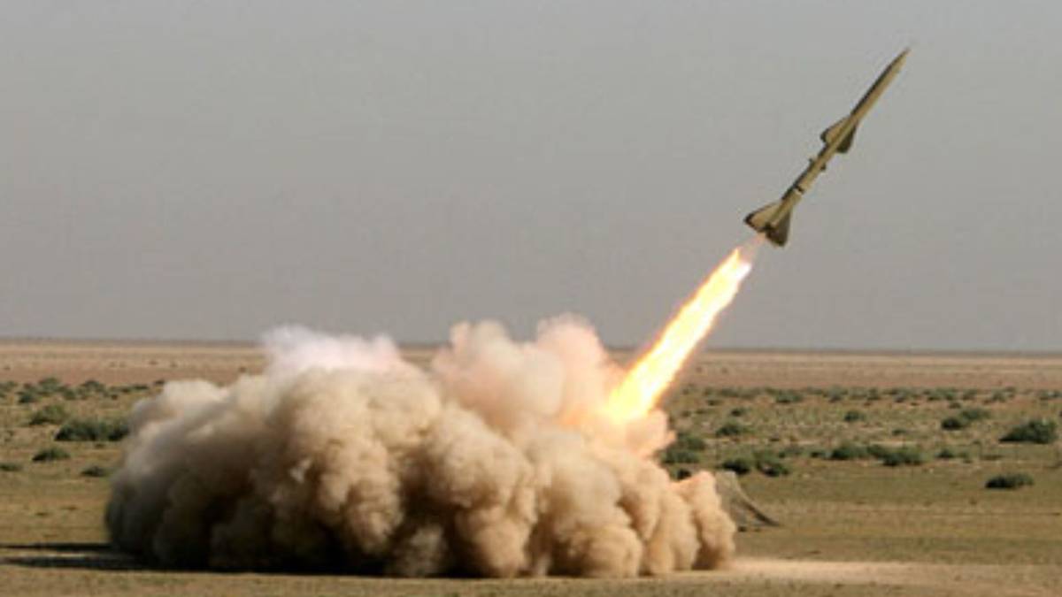 Rakieta wystrzeliwana z ziemi, pozostawiająca za sobą smugę dymu i ognia, na tle pustynnego krajobrazu.