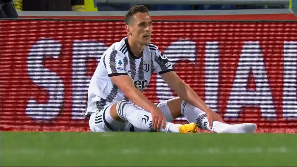 Piłkarz Arkadiusz Milik siedzi na murawie w koszulce Juventusu.