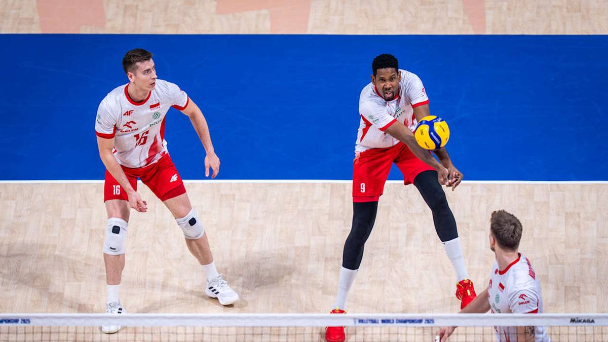 Trzech siatkarzy w białych koszulkach z czerwonymi elementami i czerwonych spodenkach podczas meczu. Dwóch zawodników z lewej strony i jeden z prawej.