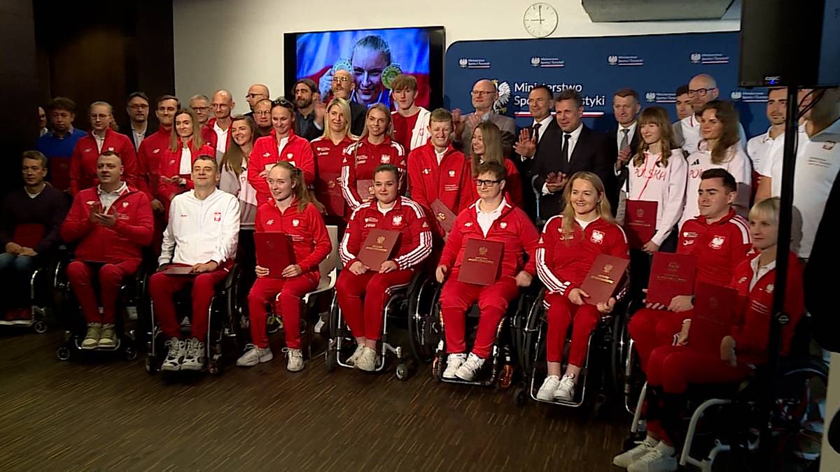 Grupa parasportowców i gości pozuje do zdjęcia w sali konferencyjnej. Medalistów uhonorowano po Mistrzostwach Świata.