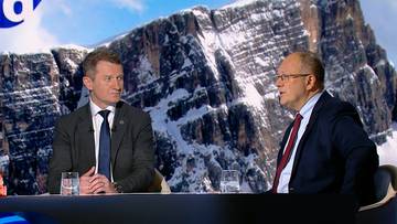 Dwóch mężczyzn w garniturach siedzi przy stole na tle ośnieżonych gór.