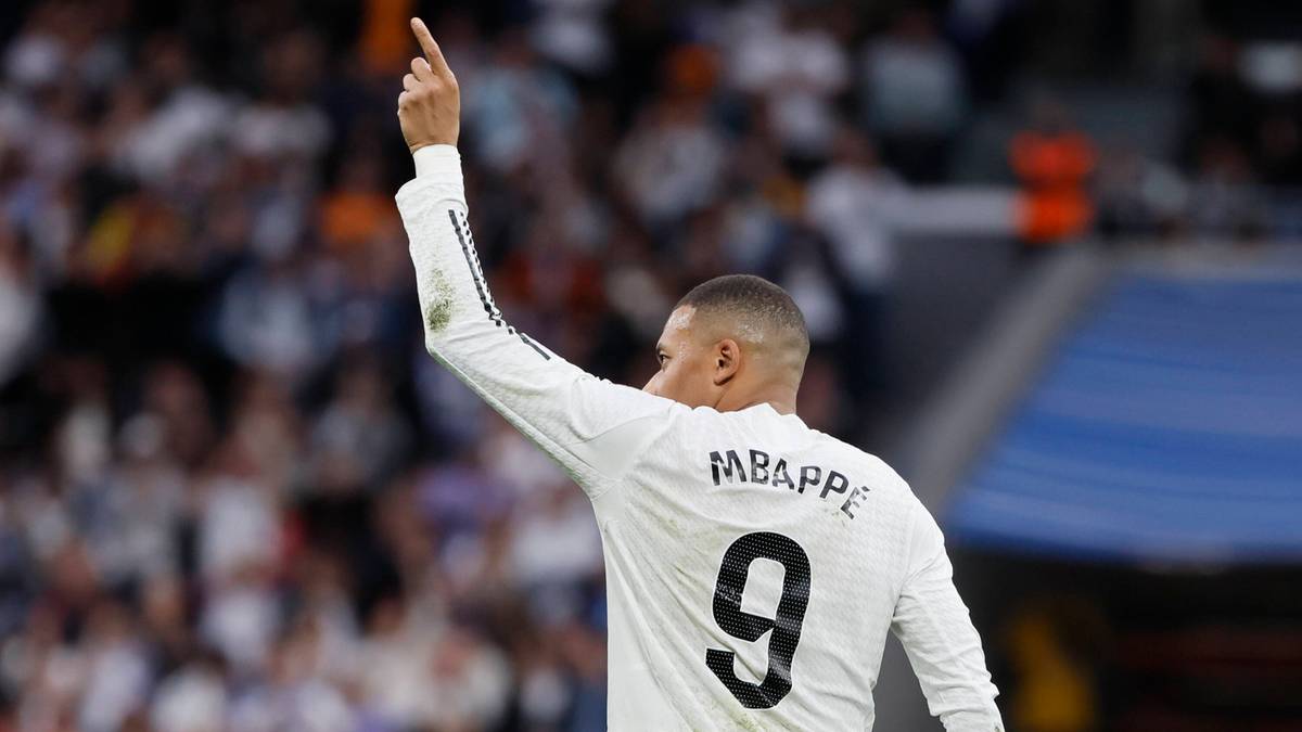 Piłkarz w białej koszulce z numerem 9 i nazwiskiem MBAPPE unosi palec wskazujący w górę.