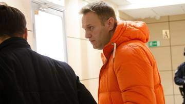 Aleksiej Nawalny w pomarańczowej kurtce, zwr&oacute;cony w prawo, z profilem widocznym dla widza.