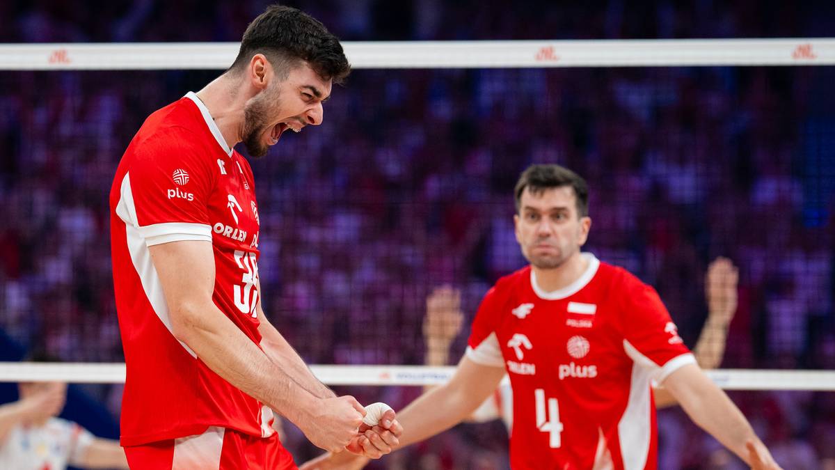 Siatkarz w czerwonej koszulce reprezentacji Polski z wykrzywioną twarzą, świętuje zdobyty punkt, trzymając za rękę kolegę z drużyny.